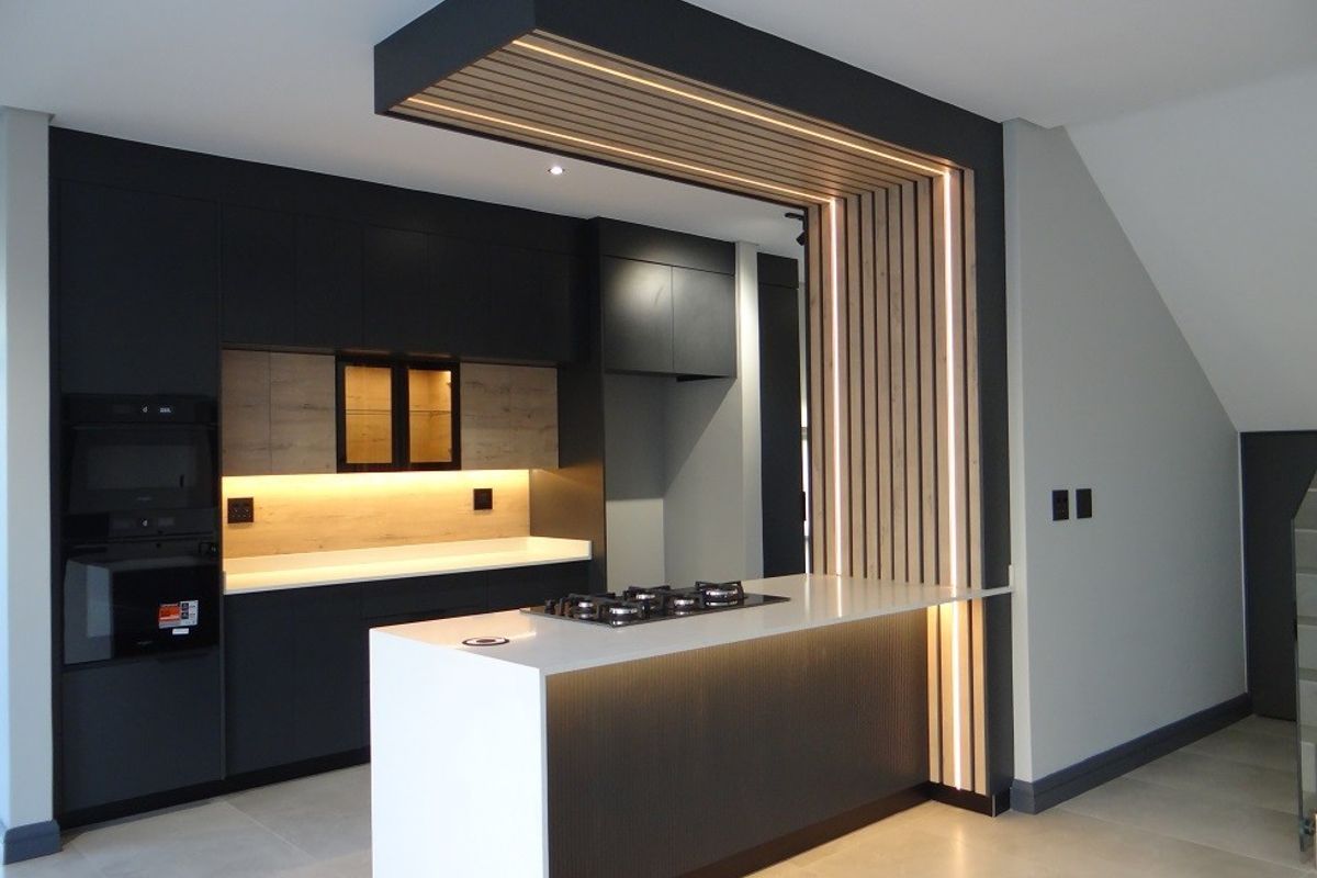 Modern kitchen featuring sleek dark cabinetry, stone countertops, a central island with a gas hob, and a striking slatted timber bulkhead with integrated lighting.