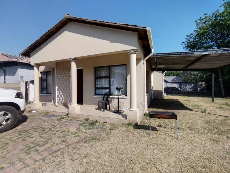 Front view of a single-story house featuring a covered porch with decorative columns, a side carport, and a paved driveway area.
