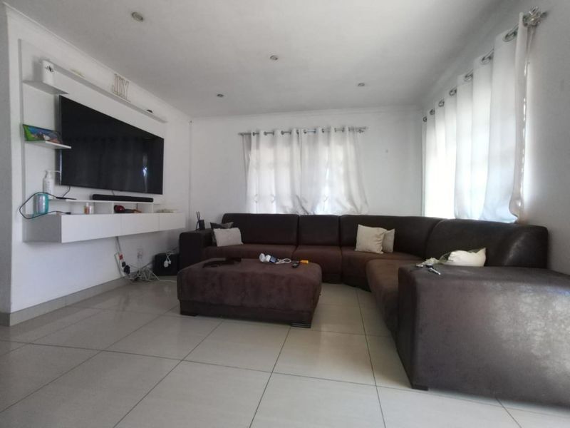 A bright living room featuring tiled flooring, recessed ceiling lights, and a built-in media console unit.