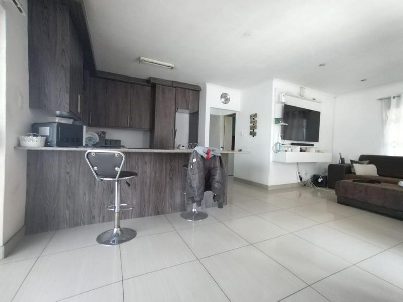 Open-plan living area featuring a modern kitchen with dark wood cabinetry, a breakfast bar, and tiled flooring, seamlessly flowing into the lounge space.