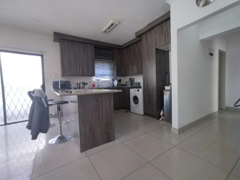 Modern kitchen featuring dark wood-look cabinetry, granite countertops, a breakfast bar, and integrated laundry facilities, finished with neutral floor tiles.