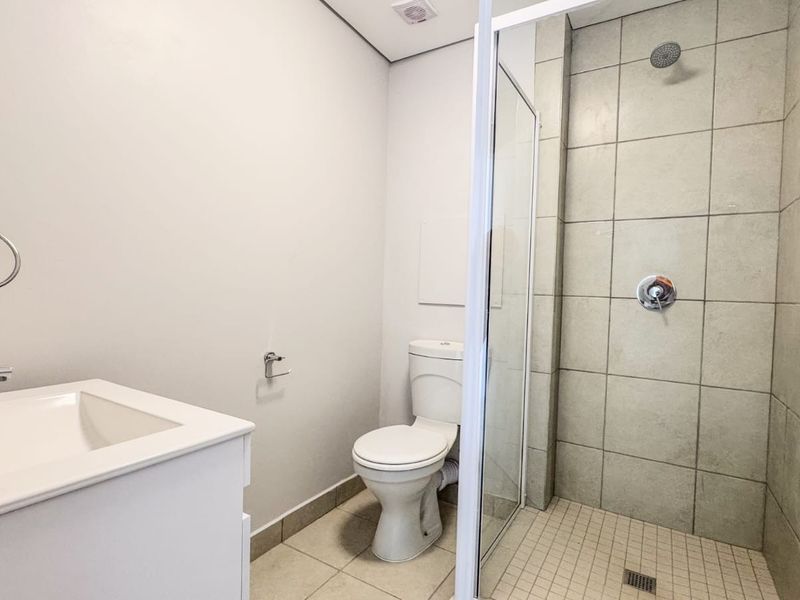 A clean and modern bathroom featuring a vanity with basin, a toilet, and a glass-enclosed shower with tiled finishes.