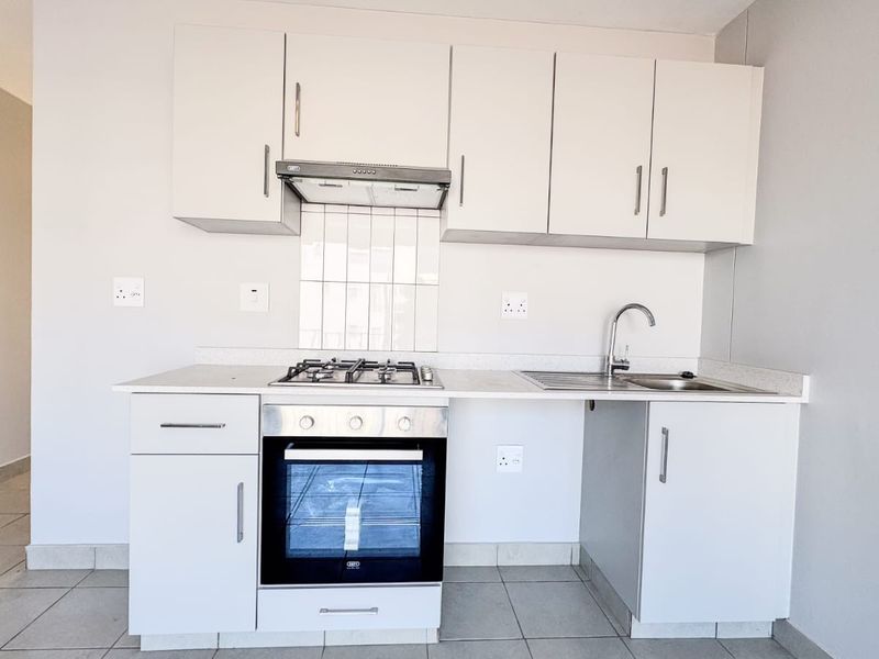 A clean and functional kitchen featuring white cabinetry, a gas hob, an electric oven, and a stainless steel sink with tiled splashback.