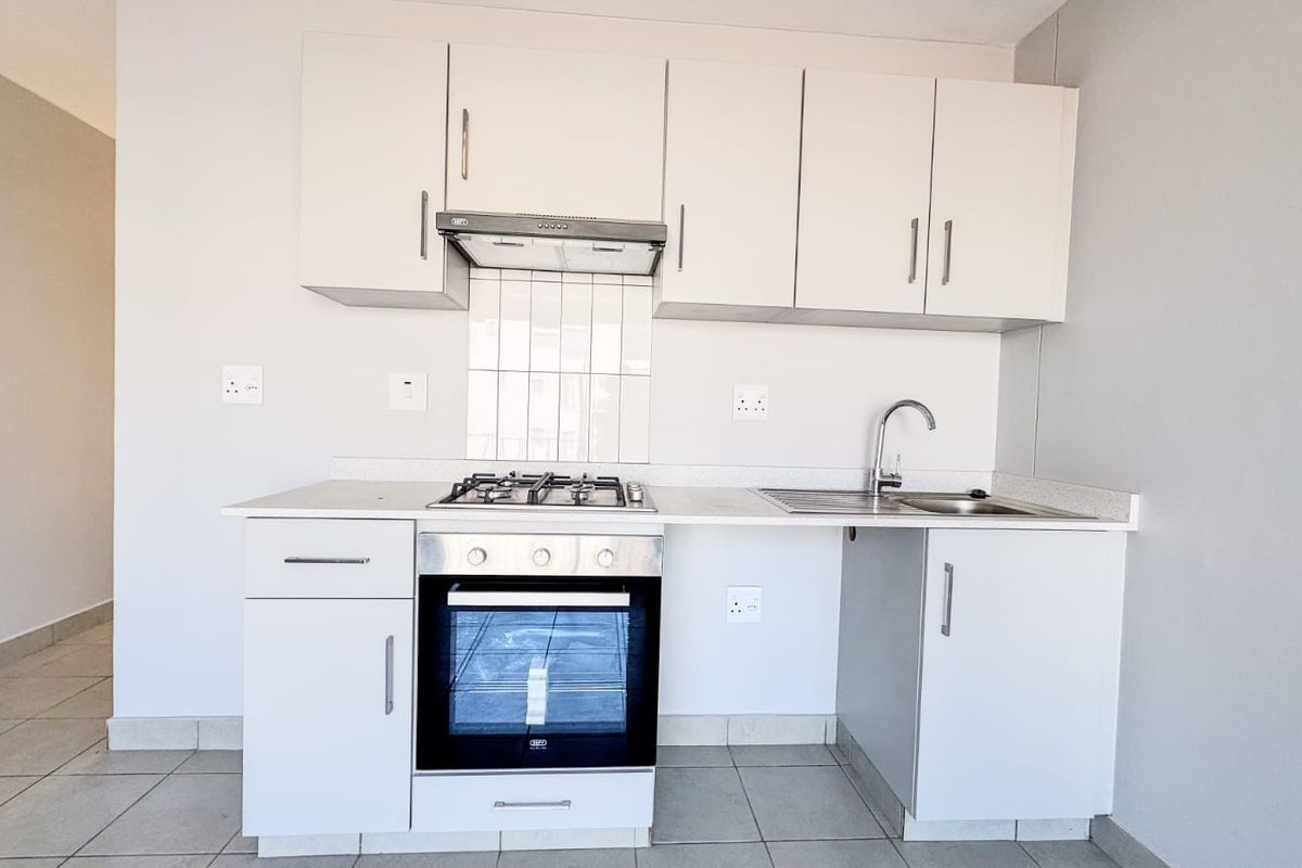 A clean and functional kitchen featuring white cabinetry, a gas hob, an electric oven, and a stainless steel sink with tiled splashback.