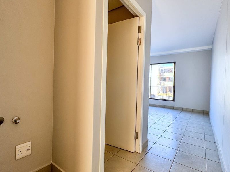 A functional laundry area featuring tiled flooring and dedicated plumbing connections, leading into an adjacent room with natural light.