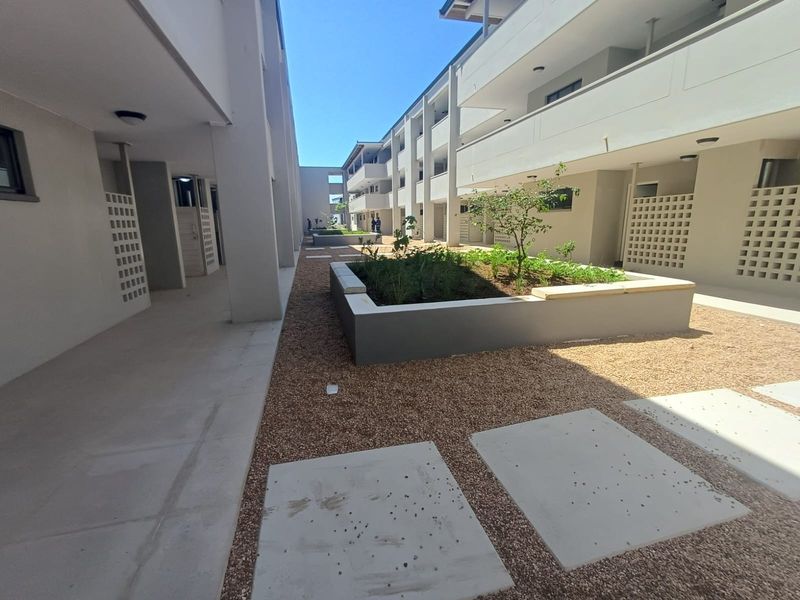 A well-maintained apartment complex courtyard featuring gravel landscaping, raised garden beds, concrete pavers, and covered walkways with breeze block architectural details.