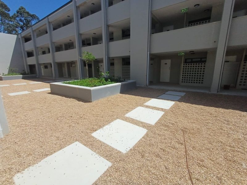 A well-maintained apartment complex courtyard featuring a gravel landscape, concrete stepping stones, and a raised garden planter box.