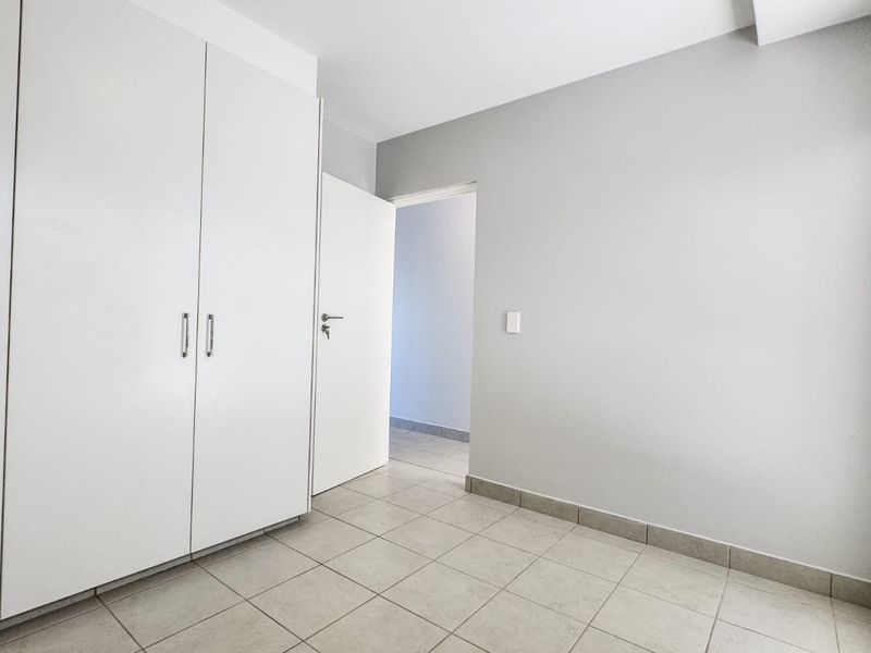 A clean, empty bedroom featuring neutral tiled flooring and ample built-in cupboard storage, ready for personalization.