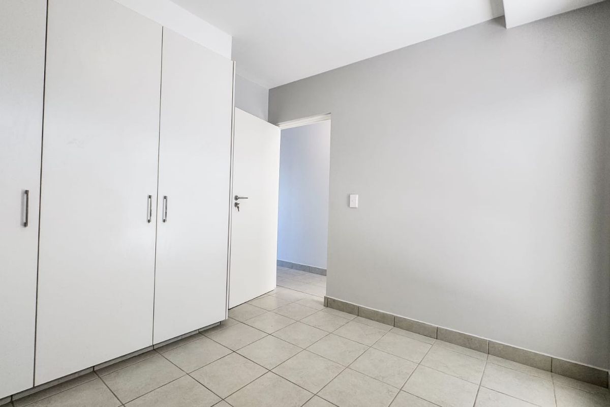 A clean, empty bedroom featuring neutral tiled flooring and ample built-in cupboard storage, ready for personalization.