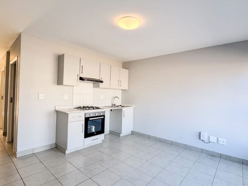 An open-plan kitchen area featuring built-in cabinetry, a gas hob, oven, and tiled flooring, offering a clean and functional space.