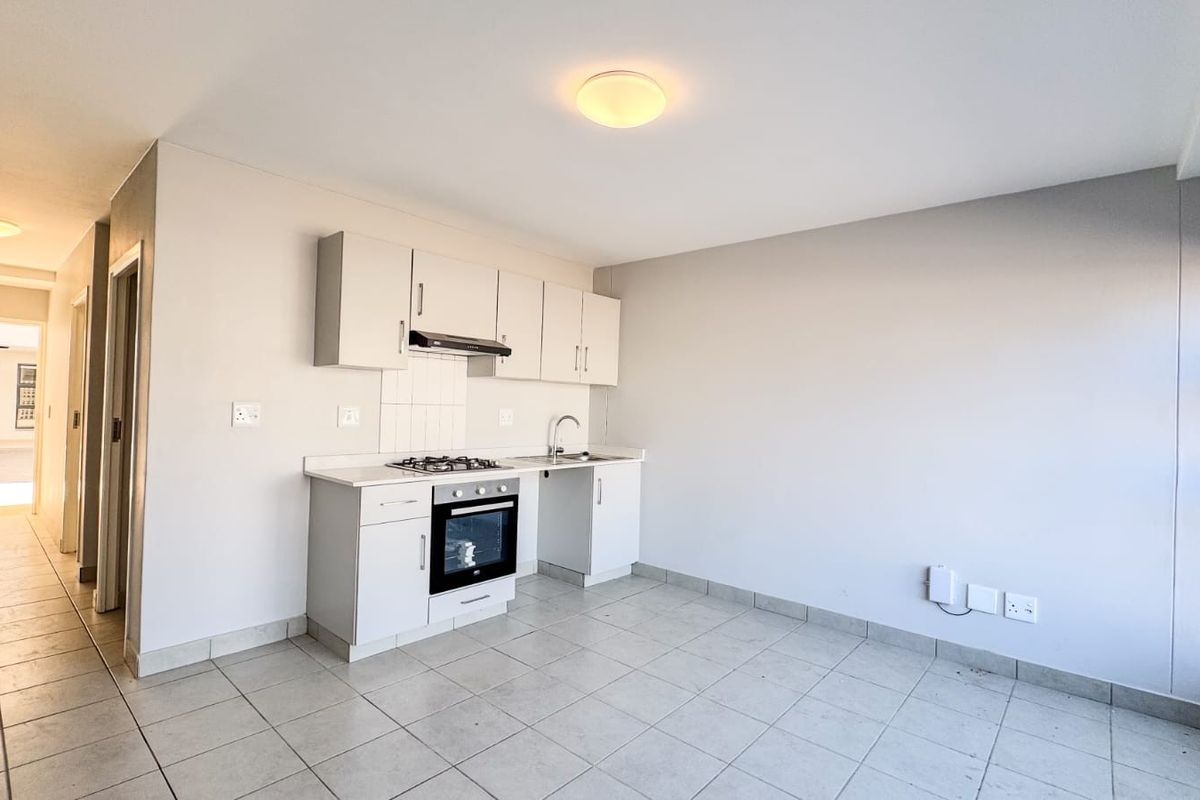 An open-plan kitchen area featuring built-in cabinetry, a gas hob, oven, and tiled flooring, offering a clean and functional space.