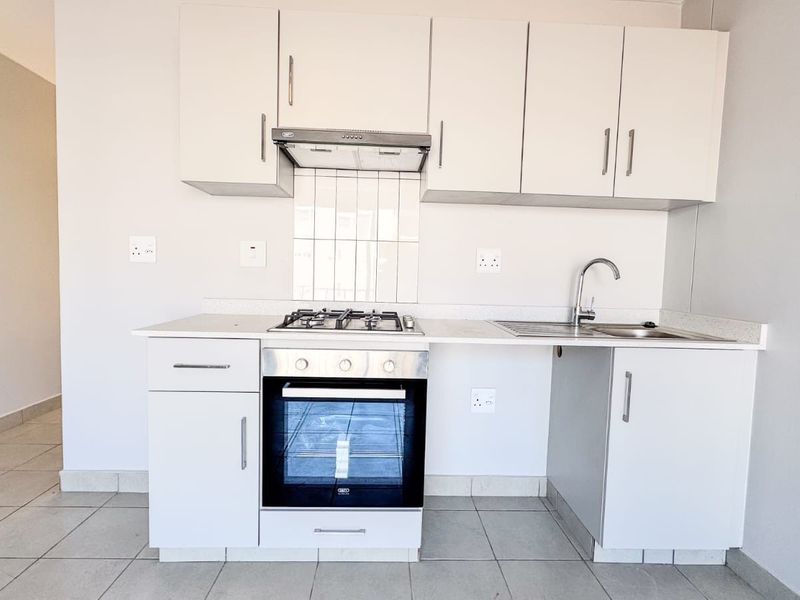 A clean, modern kitchen featuring white built-in cabinetry, a gas hob, an electric oven, and a stainless steel sink with tiled splashback.