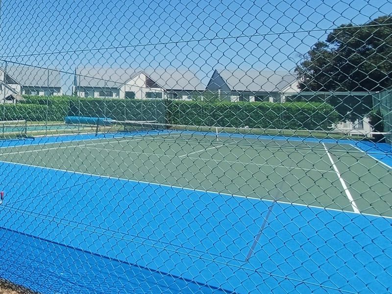 A well-maintained outdoor tennis court featuring blue and green hard court surfacing, enclosed by secure chain link fencing.