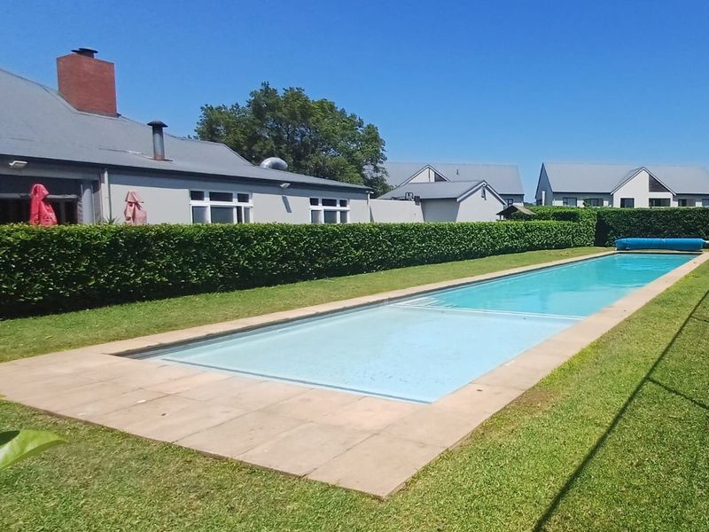 A well-maintained rectangular swimming pool set within a landscaped garden, featuring a paved surround and neatly trimmed hedge boundary.