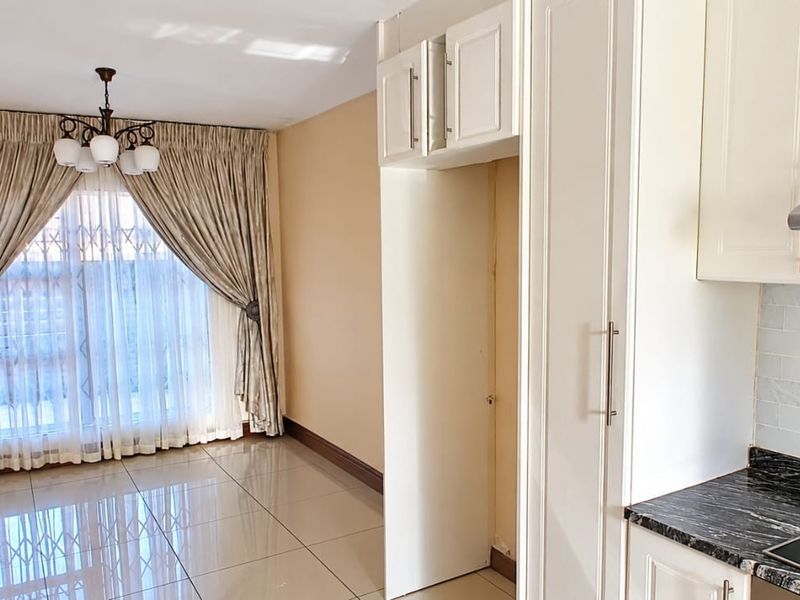 An open-plan living and kitchen area featuring tiled floors, modern white cabinetry, granite countertops, and an integrated electric hob with an extractor fan.