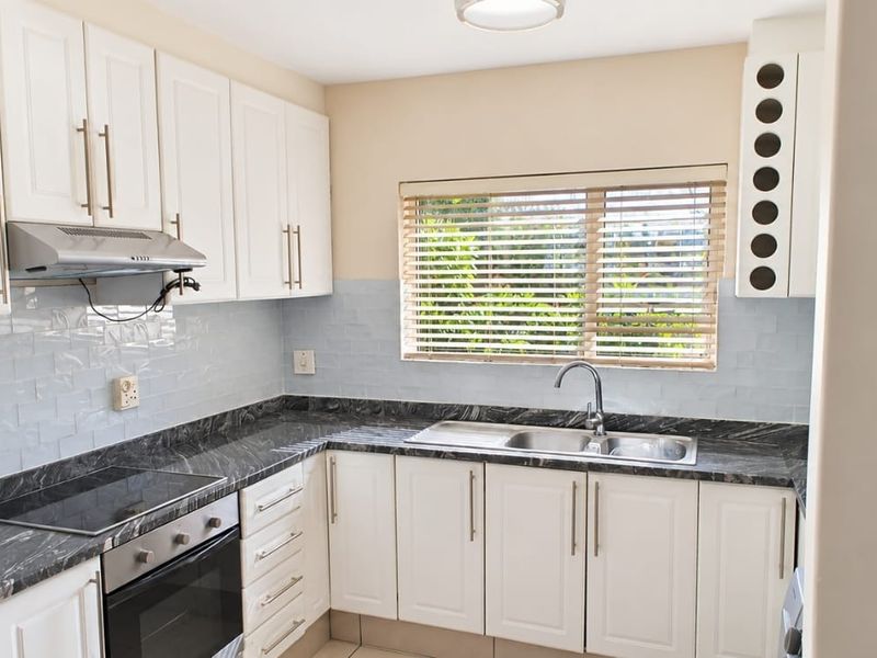 A clean, well-maintained kitchen featuring white cabinetry, dark marble-effect countertops, a stainless steel sink, and integrated cooking appliances.