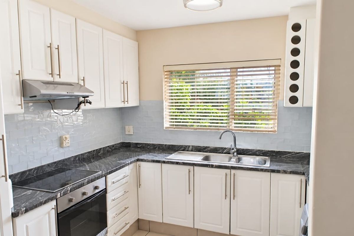 A clean, well-maintained kitchen featuring white cabinetry, dark marble-effect countertops, a stainless steel sink, and integrated cooking appliances.