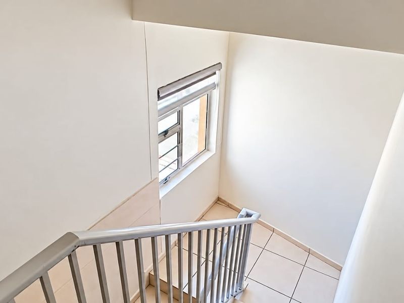 A clean and well-maintained staircase area featuring tiled flooring, neutral walls, and a secure metal balustrade.