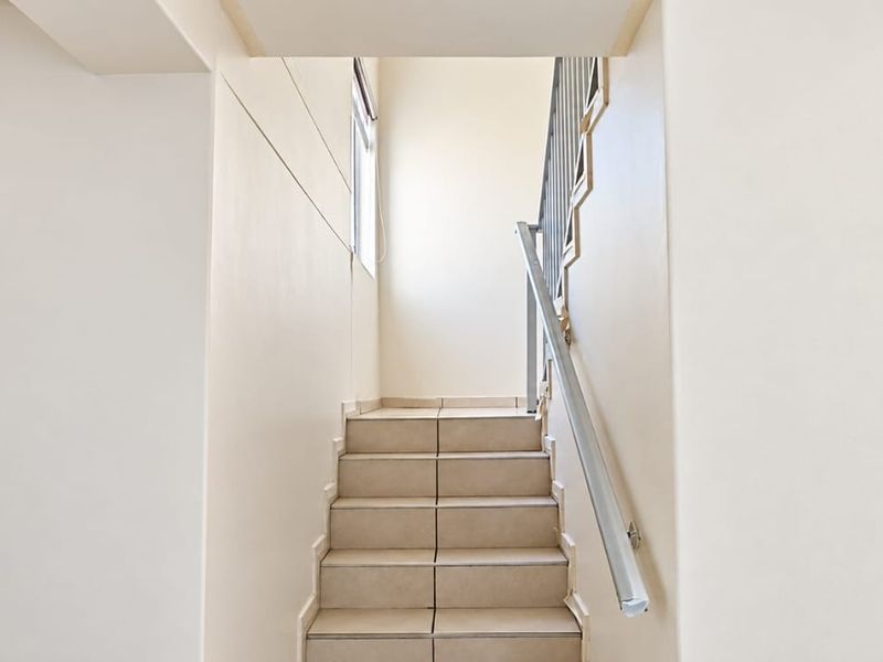 A clean, minimalist staircase featuring tiled steps and a simple metal handrail, providing a bright and functional transition between levels.