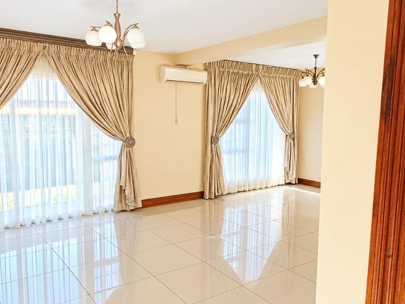 Spacious, light-filled living area featuring polished tiled flooring, split-system air conditioning, and large windows dressed with elegant curtains.