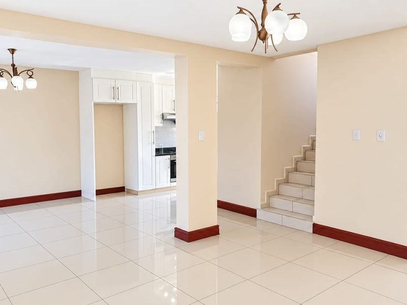 Spacious open-plan living area featuring tiled floors, a staircase, and a functional kitchen layout with built-in cabinetry, offering a bright and neutral living space.