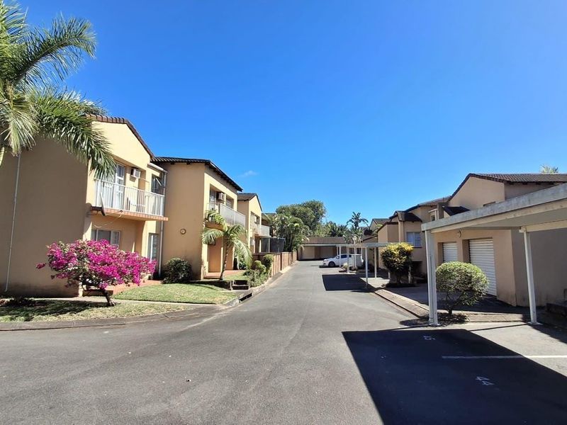 A view of the residential complex driveway featuring multiple units with balconies, carports, and garage access.