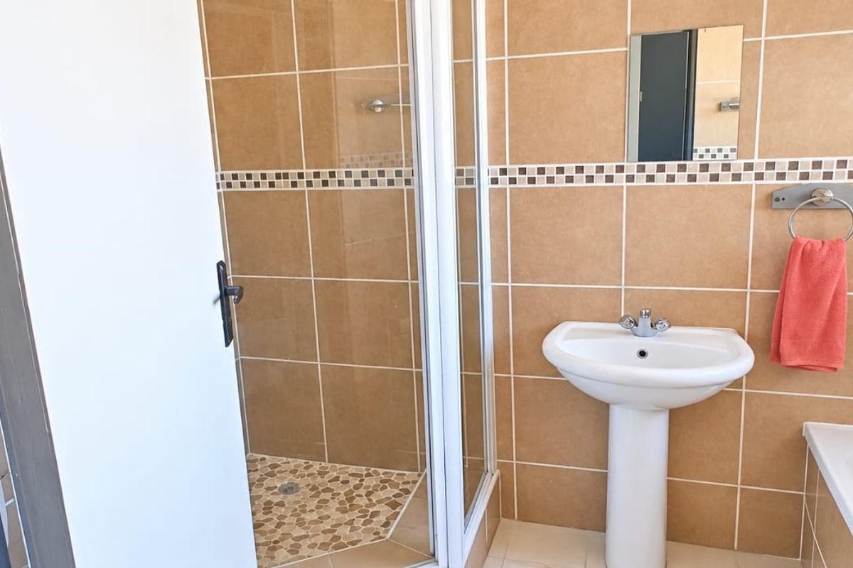 A functional bathroom featuring a pedestal basin, a separate shower enclosure with pebble-style flooring, and a bathtub with tiled wall finishes.