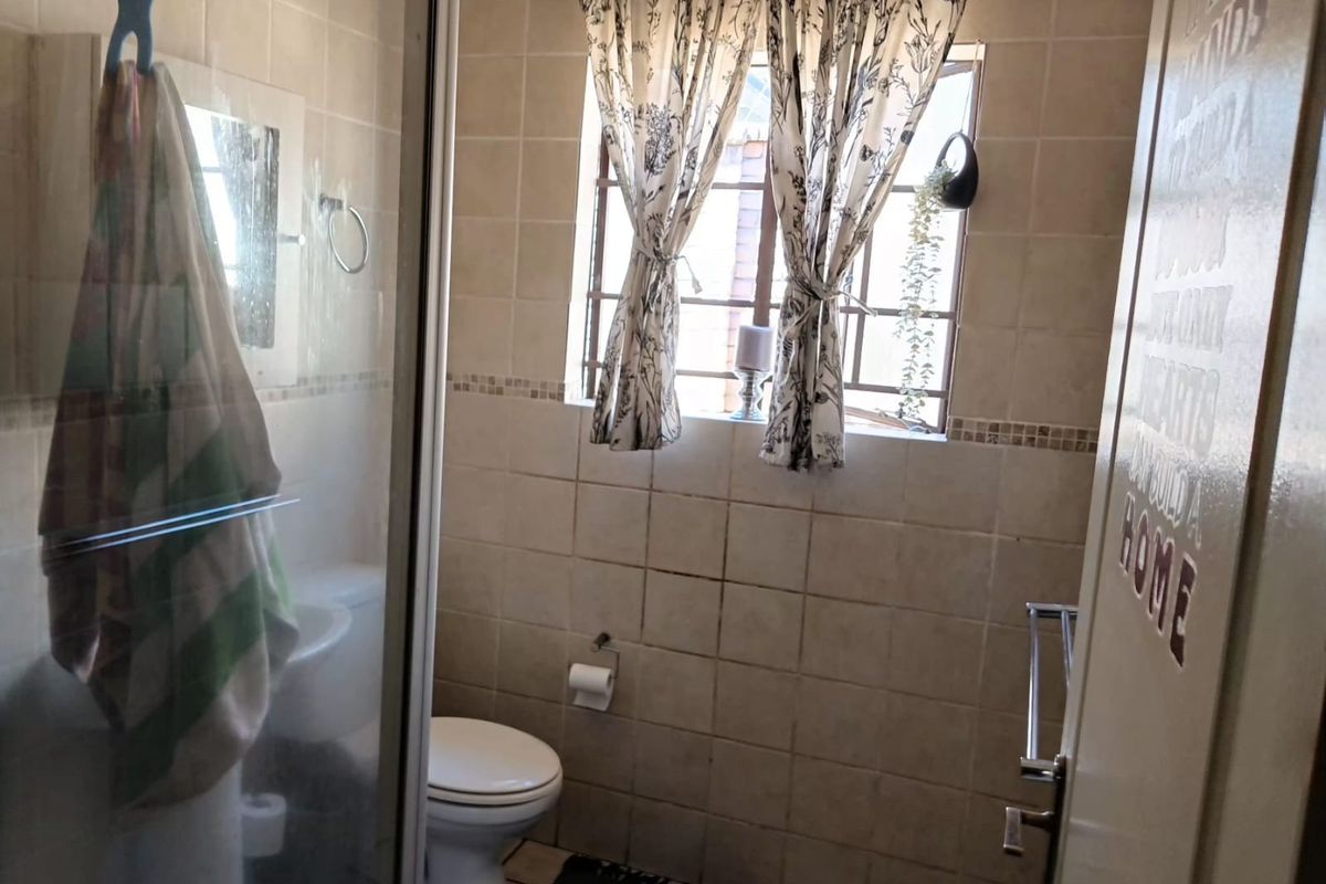 A functional bathroom featuring a shower enclosure, toilet, and neutral wall and floor tiling.