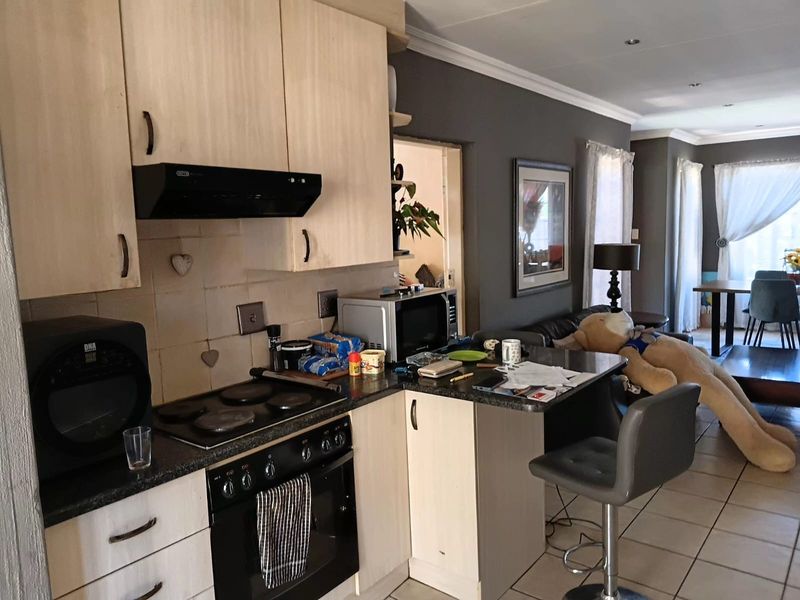 Open-plan kitchen and living area featuring light wood cabinetry, dark countertops, built-in oven and hob, and tiled flooring throughout.