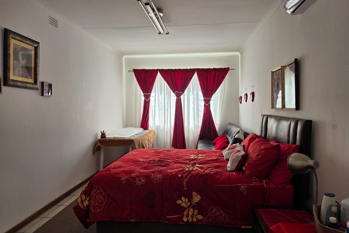 A functional bedroom featuring tiled flooring, an installed air conditioning unit, and large window with curtain rails.