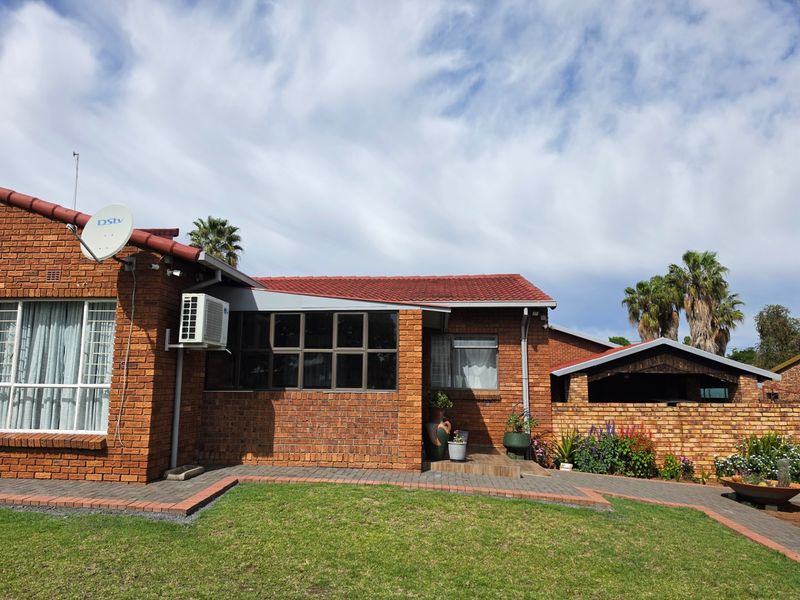 A well-maintained face brick rear exterior featuring a tiled roof, aluminium window frames, an integrated air conditioning unit, and a paved garden walkway.