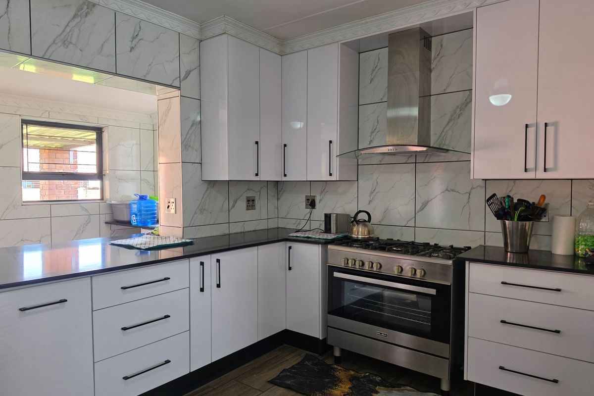 Modern kitchen featuring white gloss cabinetry, marble-look wall tiling, black stone countertops, and a stainless steel gas stove with extractor fan.