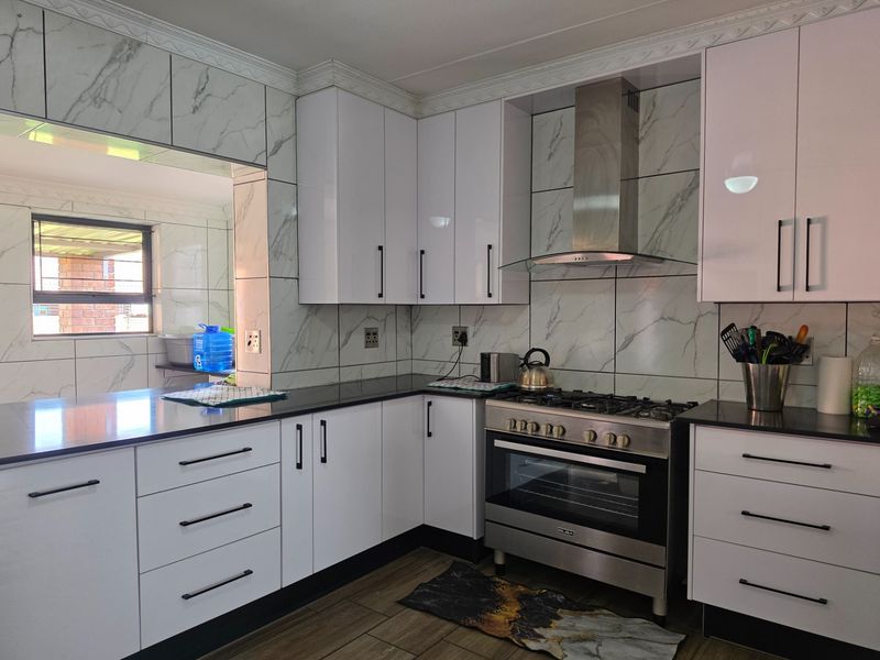 Modern kitchen featuring white gloss cabinetry, marble-look wall tiling, black stone countertops, and a stainless steel gas stove with extractor fan.