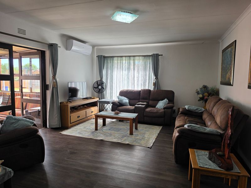 A well-maintained living room featuring dark laminate flooring, an air conditioning unit, and large sliding glass doors providing access to the patio.