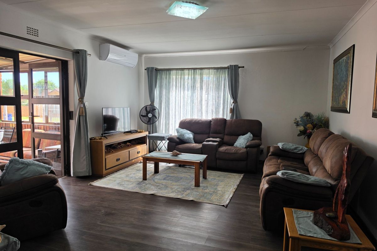 A well-maintained living room featuring dark laminate flooring, an air conditioning unit, and large sliding glass doors providing access to the patio.