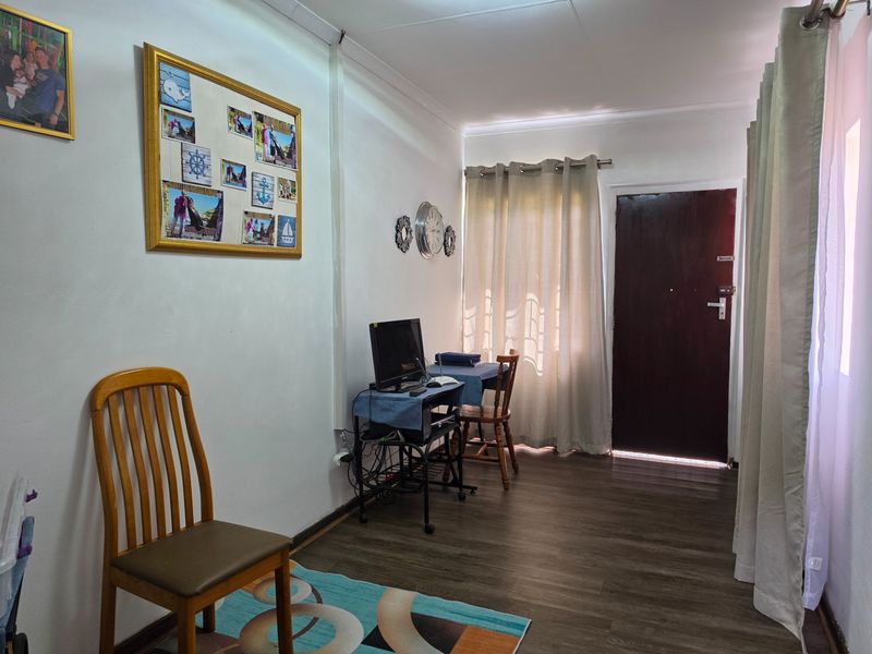 A functional living area featuring laminate flooring, neutral wall finishes, and direct access to an exterior door with natural light filtering through curtains.