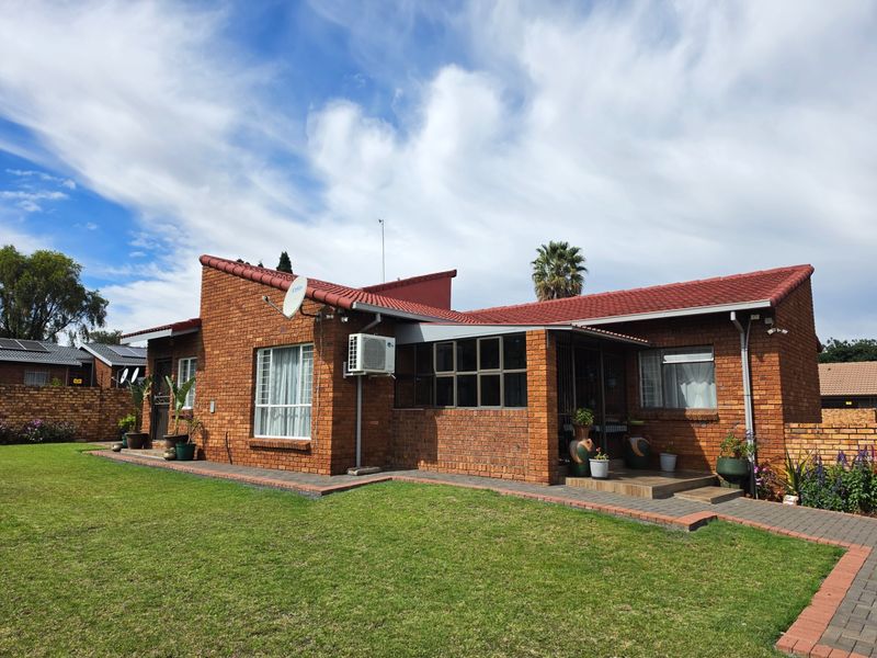 A well-maintained face brick house featuring a tiled roof, aluminium window frames, and a neat paved walkway leading to the rear garden area.