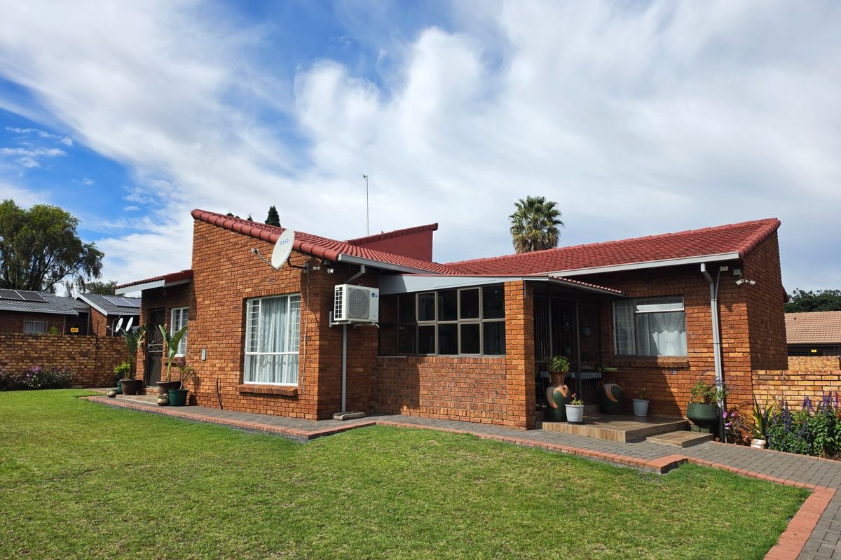 A well-maintained face brick house featuring a tiled roof, aluminium window frames, and a neat paved walkway leading to the rear garden area.