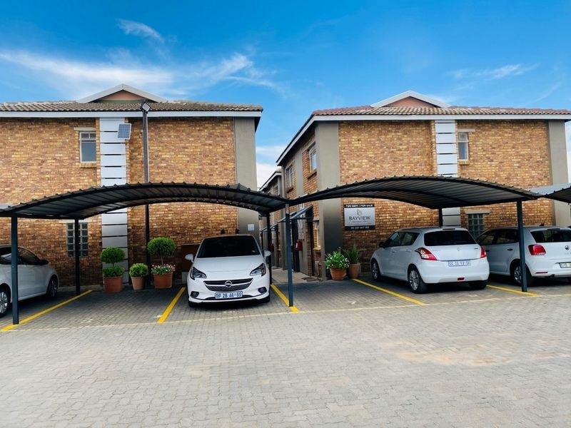 Front exterior view of the townhouse complex featuring brick facades, covered carports, and paved parking areas.