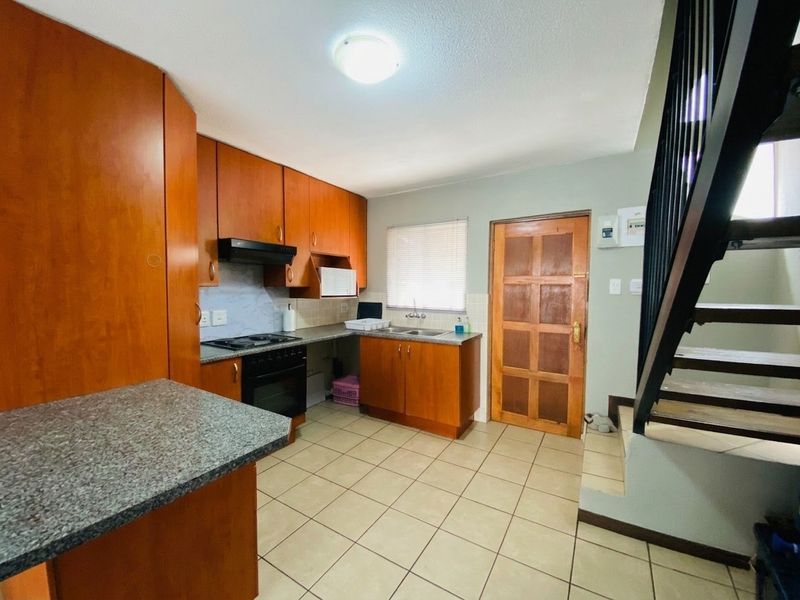 A functional kitchen featuring wooden cabinetry, laminate countertops, built-in oven with extractor fan, and tiled flooring, conveniently located adjacent to the staircase.