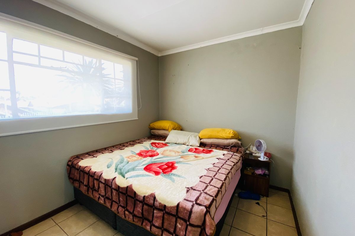 A functional bedroom featuring tiled flooring, neutral wall tones, and a large window with a roller blind.