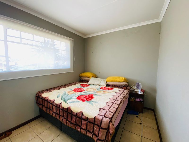 A functional bedroom featuring tiled flooring, neutral wall tones, and a large window with a roller blind.