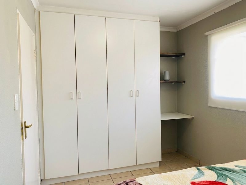 A bedroom featuring a large white built-in wardrobe, integrated shelving, a built-in desk area, and neutral tiled flooring.