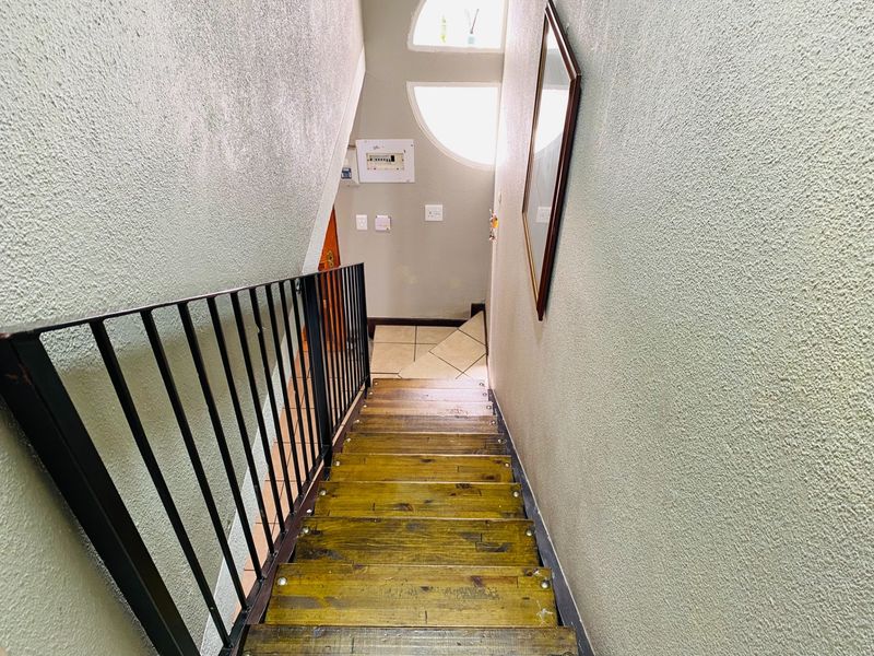 A narrow staircase with metal balustrades leading to a landing area featuring tiled floors and arched windows.