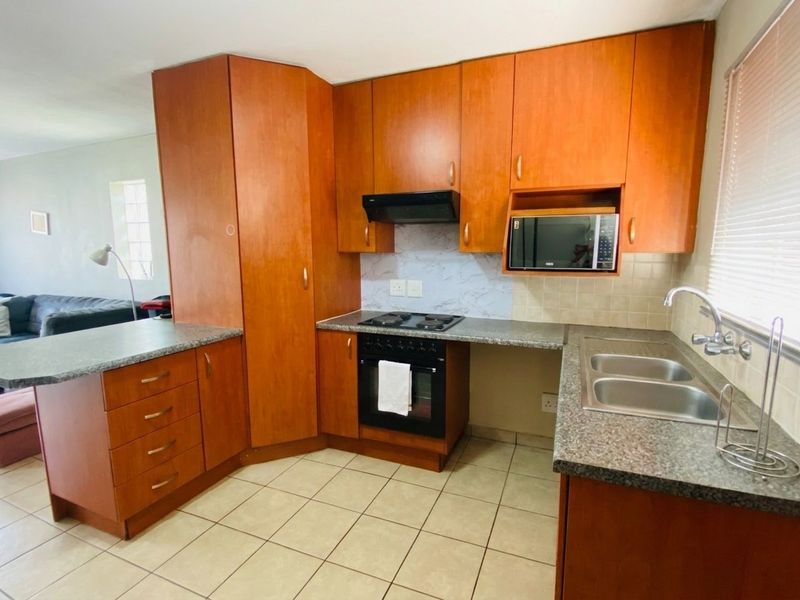 Functional kitchen featuring wood-finish cabinetry, granite-look laminate countertops, a double sink, and integrated cooking appliances with tiled flooring and backsplash.