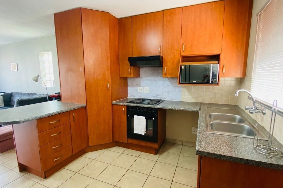 Functional kitchen featuring wood-finish cabinetry, granite-look laminate countertops, a double sink, and integrated cooking appliances with tiled flooring and backsplash.