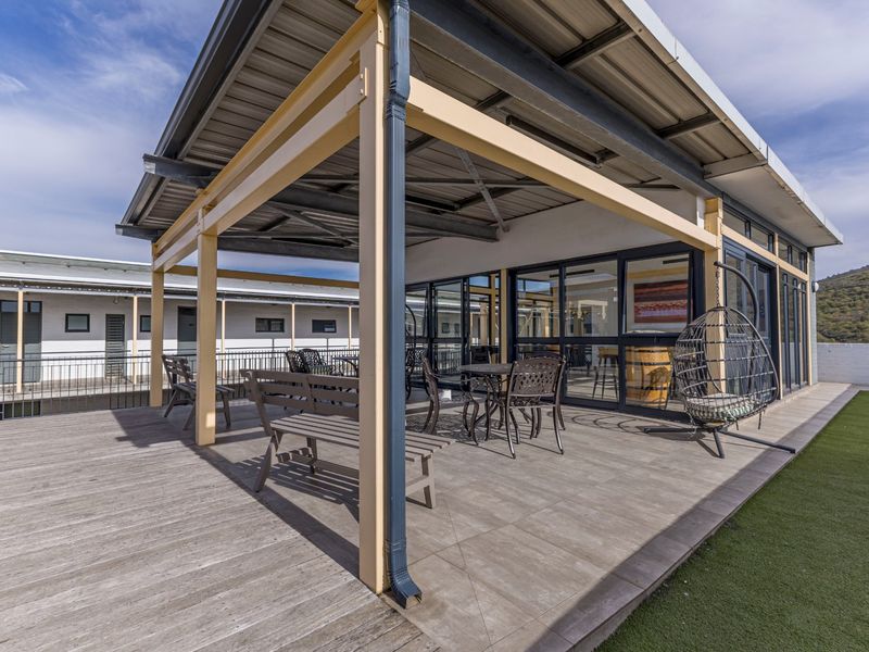 Spacious covered patio featuring a mix of timber decking and tiled flooring, enclosed by metal railings and large sliding glass doors.