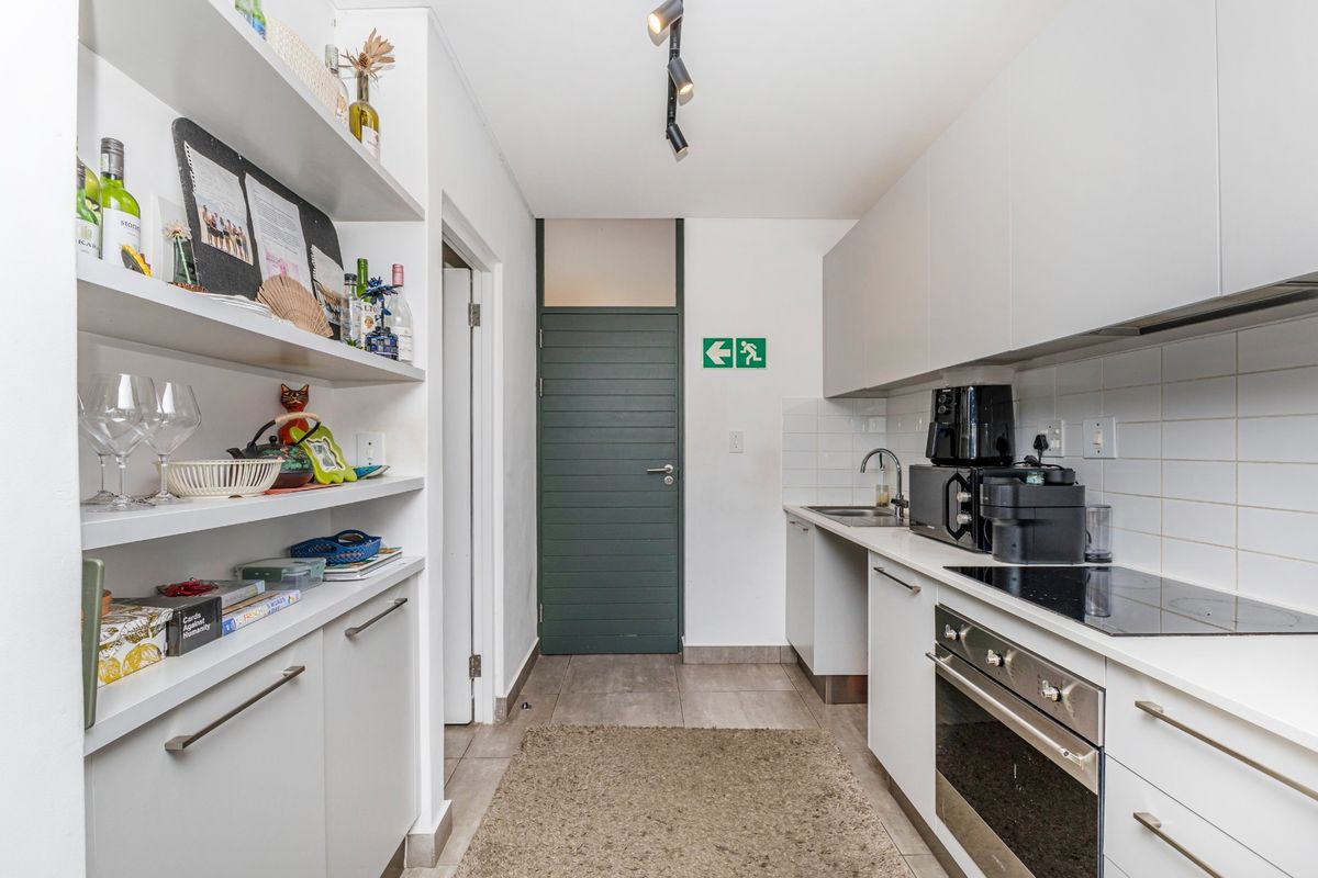 A compact, modern kitchen featuring white cabinetry, built-in oven and hob, tiled backsplash, and integrated shelving for storage.