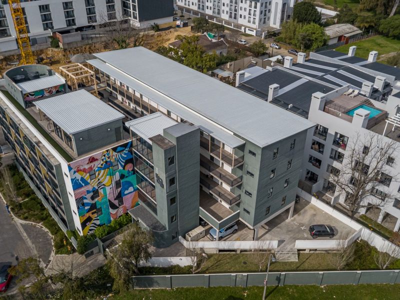 Aerial view of a modern multi-story apartment complex featuring a distinctive mural, private balconies, and an on-site parking area.