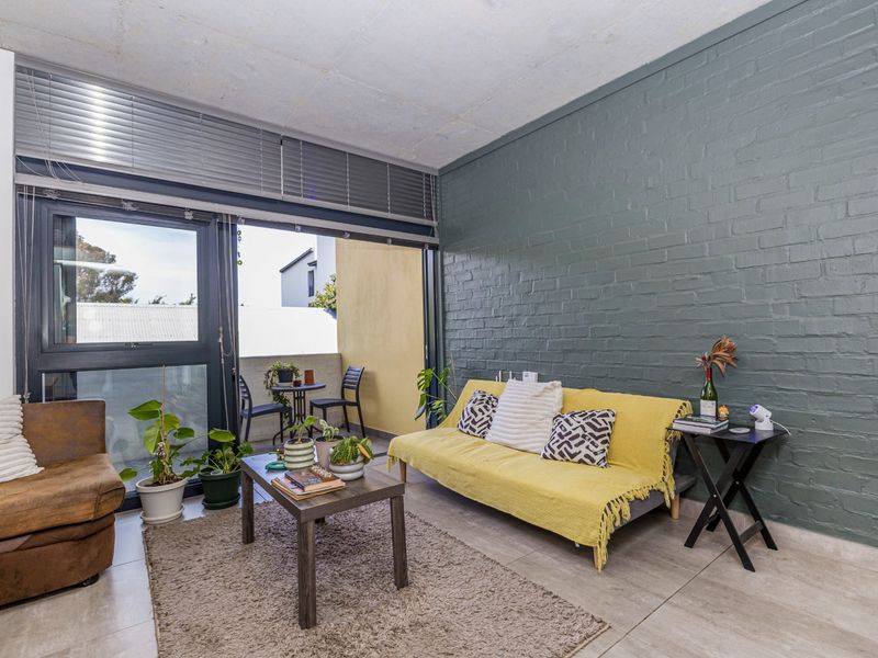 Living room featuring an exposed concrete ceiling, a painted brick feature wall, and large sliding glass doors leading to a private balcony.